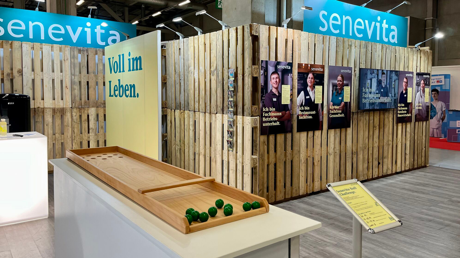 Senevita-Messestand mit Holzoptik, Schautafeln zu verschiedenen Berufen und einer interaktiven Ball-Challenge.