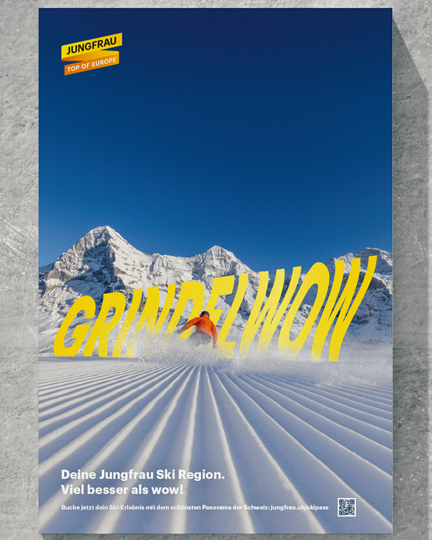 Plakat mit gelbem Schriftzug ‚GRINDELWOW‘ vor verschneiter Bergkulisse in der Jungfrau Ski Region