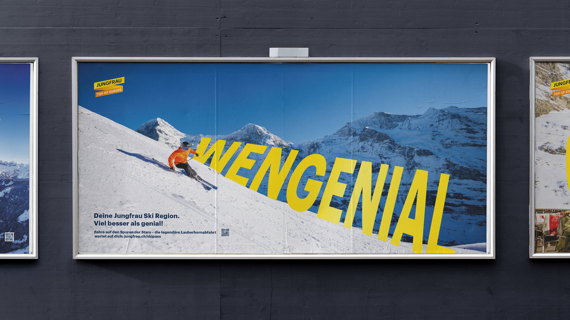 Plakat mit dem gelben Schriftzug ‚WENGENIAL‘ vor verschneiter Bergkulisse; Skifahrer in orangener Jacke fährt die Piste hinunter.