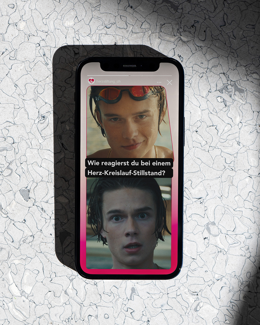 Smartphone auf einem hell gemusterten Untergrund mit einem Video, das zwei Gesichtsausdrücke eines jungen Mannes zeigt und dem Text „Wie reagierst du bei einem Herz-Kreislauf-Stillstand?“.