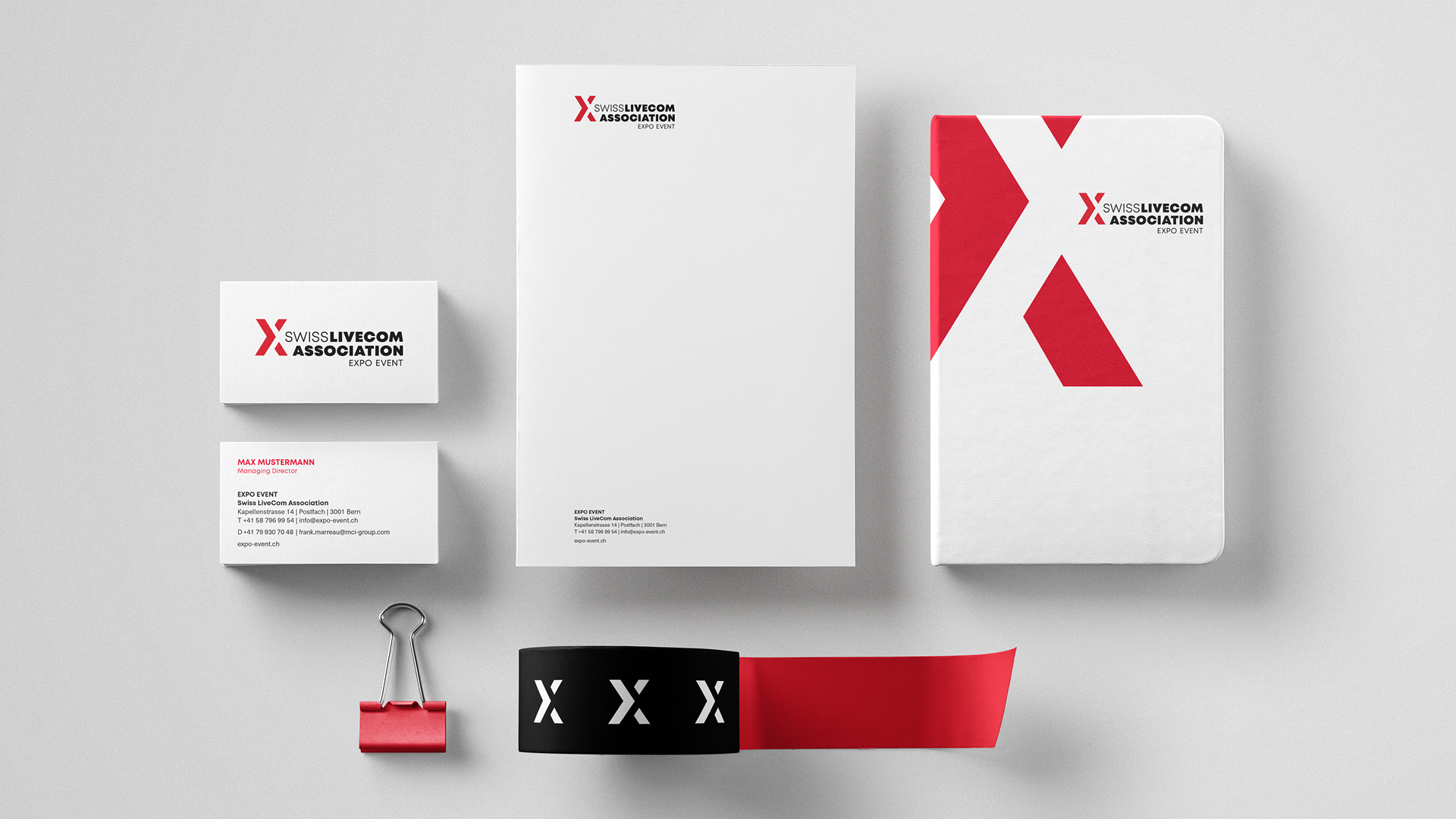 Geschäftsausstattung der Swiss LiveCom Association mit Briefpapier, Visitenkarten, Ordner, Büroklammer und Band in Weiss, Rot und Schwarz mit X-Logo.